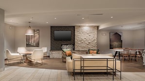 Een moderne woonkamer met een stenen accentmuur, een flatscreen televisie en een eethoek met houten stoelen.