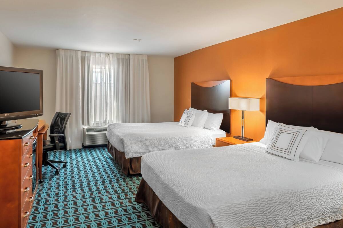 A hotel room with two beds, a desk with a computer, a chair, and a window with curtains.