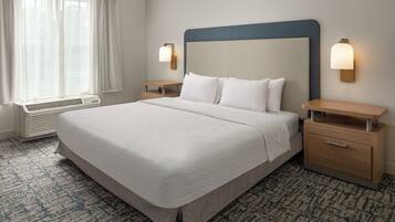 A hotel room with a large bed, bedside tables, a heater, and a window with curtains.
