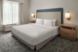 Una habitación de hotel con una cama grande, mesitas de noche, un calentador y una ventana con cortinas.
