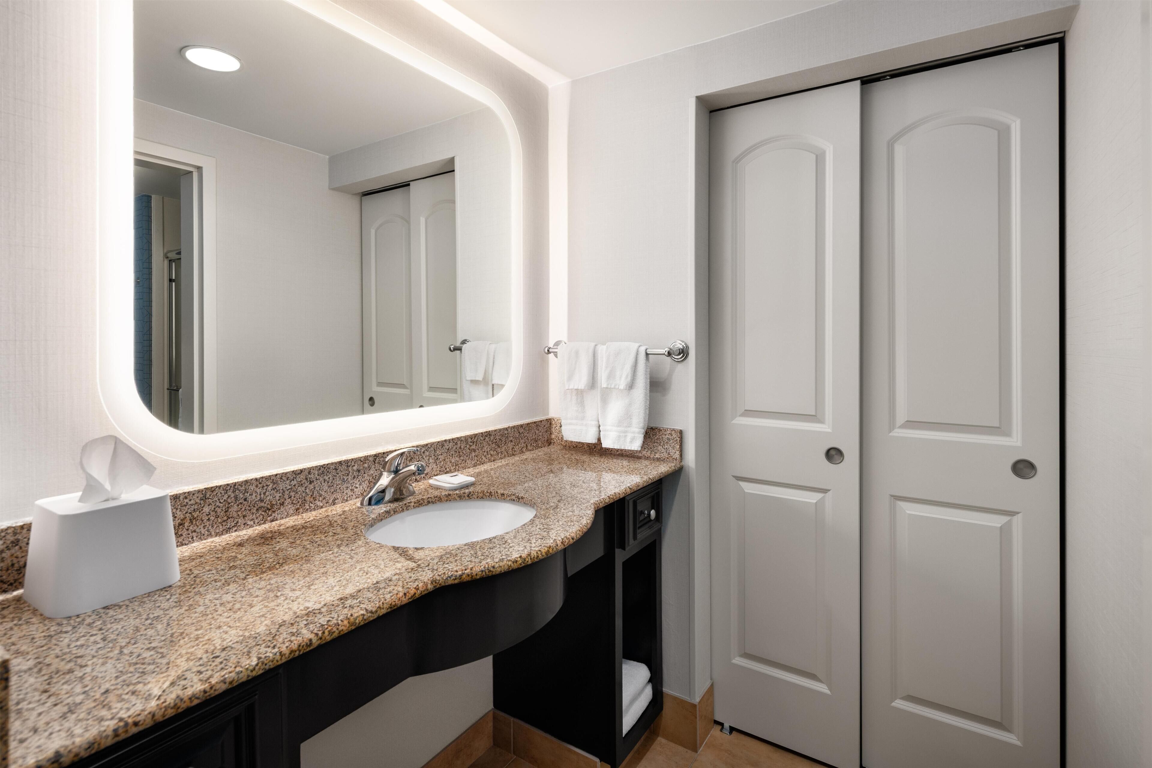 A bathroom with a granite countertop, a white sink, a mirror, and a door.