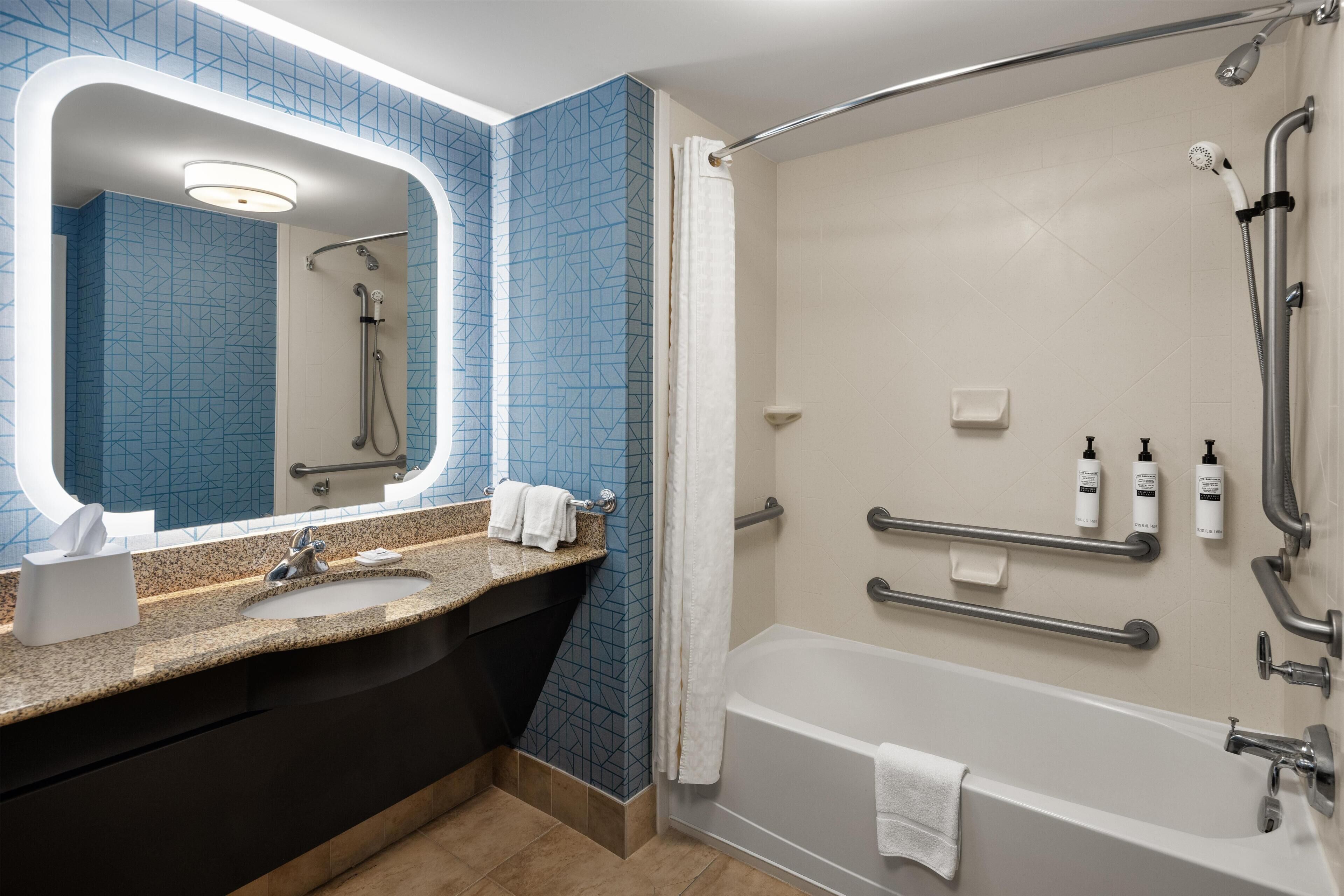 Ein modernes Badezimmer mit einer Granit-Arbeitsplatte, einem großen Spiegel, einer Badewanne und einer Duschkabine.