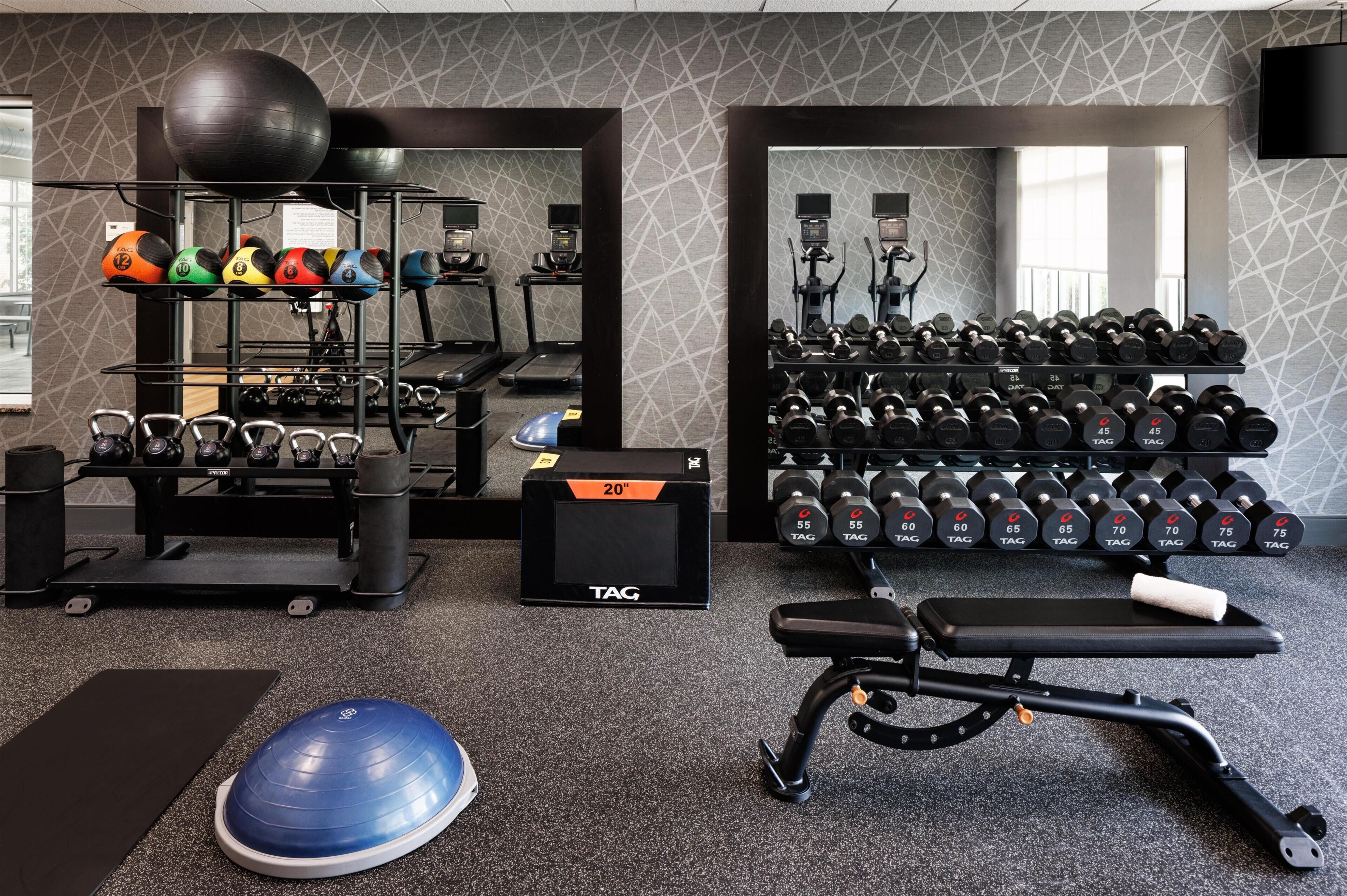 Un gimnasio con equipo de ejercicio, incluyendo cintas de correr, kettelbells y mancuernas.
