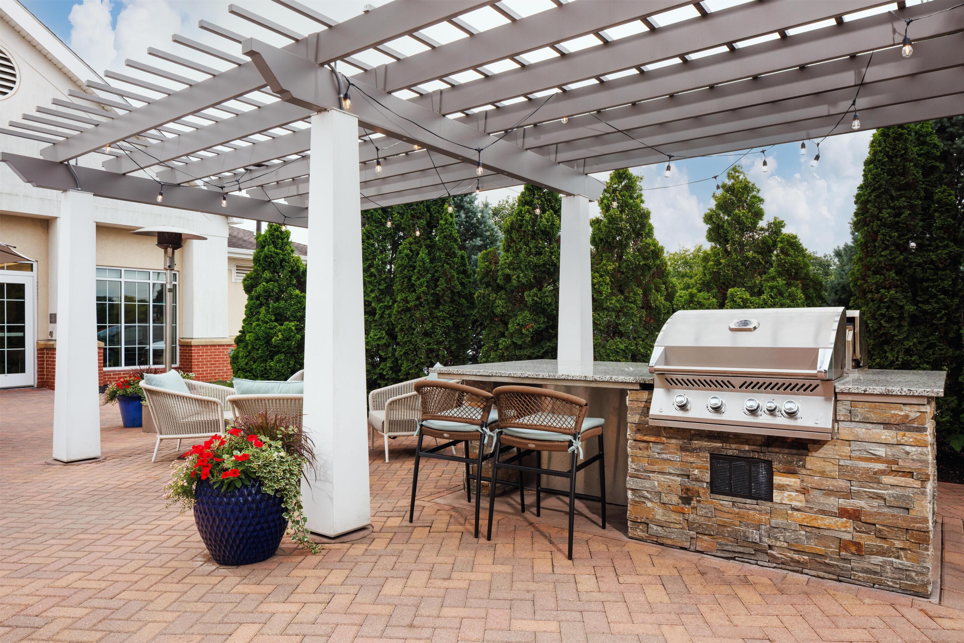 An outdoor patio with a grill, seating, and a pergola structure.