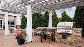 An outdoor patio with a grill, seating, and a pergola structure.