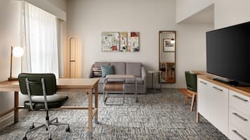 A modern living room with a sofa, a television, a desk with a chair, and a patterned carpet.