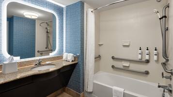 A modern bathroom with a granite countertop, a large mirror, a bathtub, and a shower area.