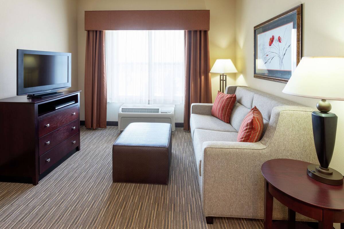 A hotel room with a flat-screen TV, a sofa, a small table, a lamp, and a framed picture on the wall.