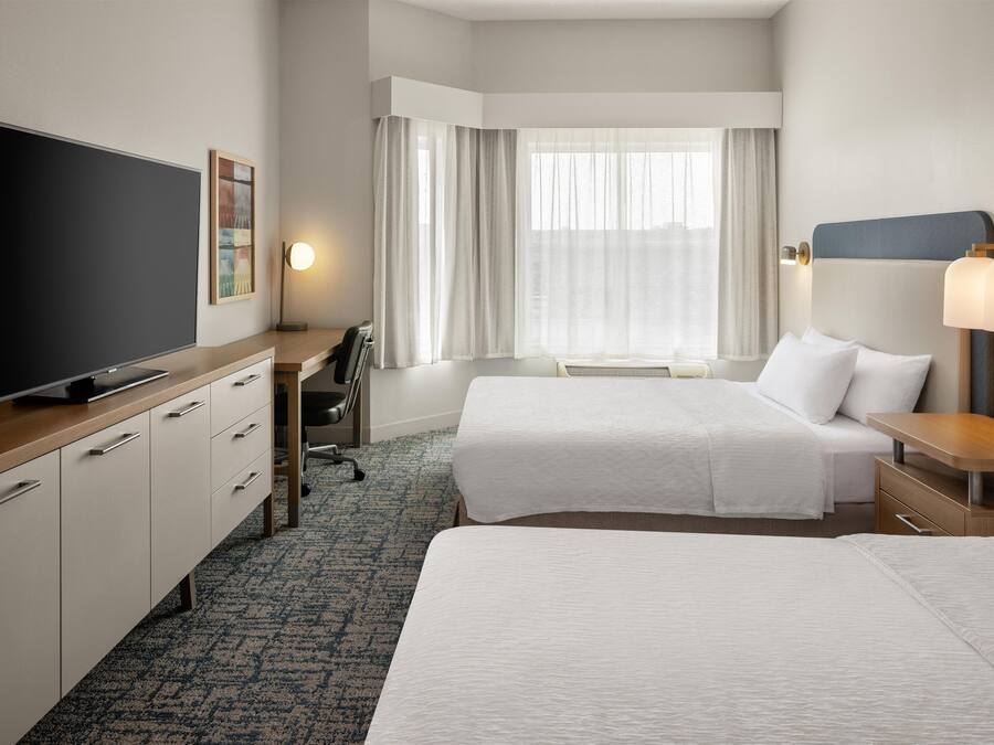 Une chambre d’hôtel avec deux lits, un bureau, une télévision et une fenêtre avec des rideaux.