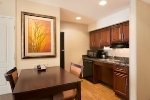 A compact kitchen with wooden cabinets, a microwave, a coffee maker, and a dining table with chairs.