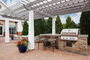 Un patio al aire libre con una parrilla, asientos y una estructura de pérgola.