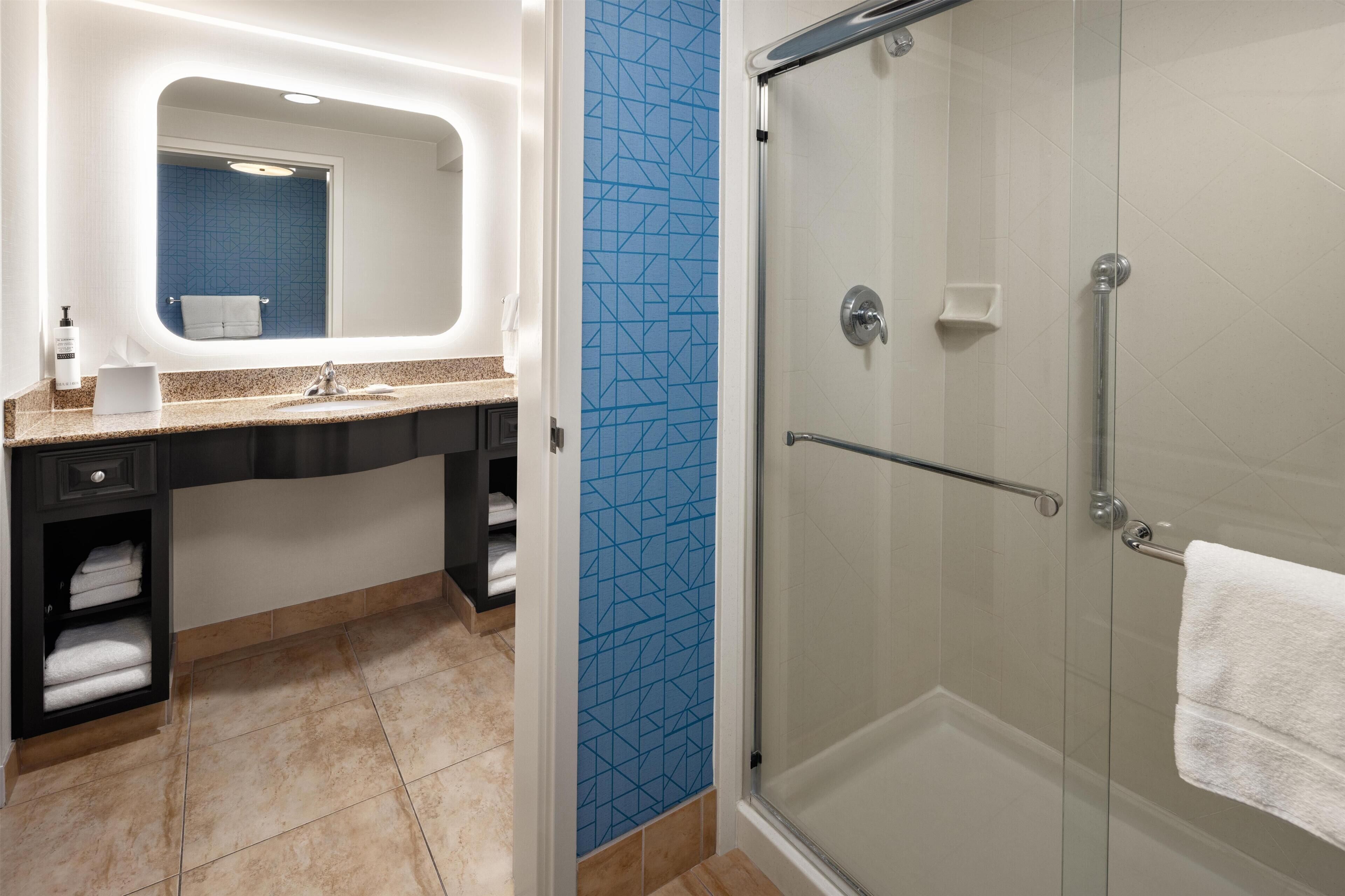 A bathroom with a shower, sink, and a towel rack.