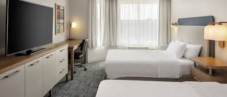 A hotel room with two beds, a desk, a television, and a window with curtains.