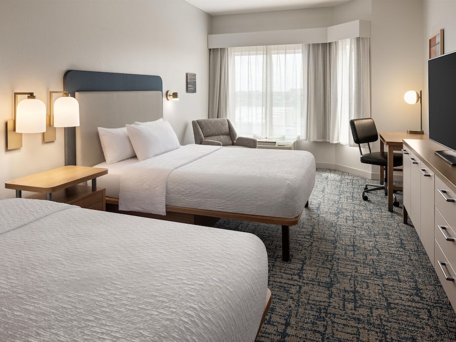 A hotel room with two beds, a desk, a chair, a television, and a window with curtains.