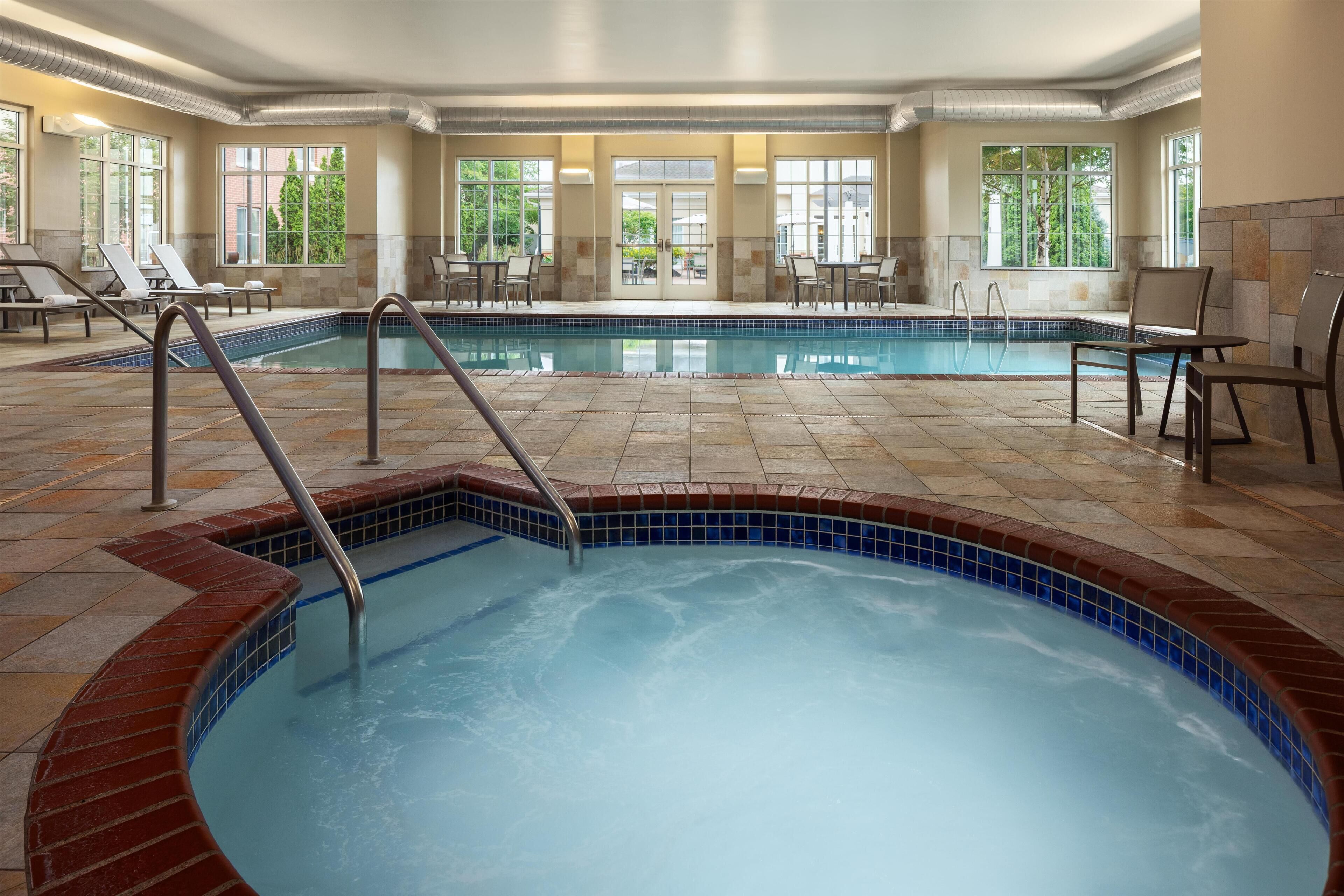 Ein Hotelpoolbereich mit zwei Pools, davon einer mit einem Whirlpool, sowie Sitzbereichen inklusive Tischen und Stühlen.