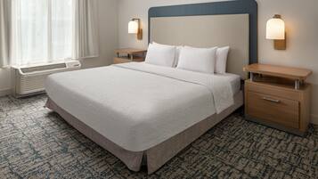 A hotel room with a large bed, bedside tables, a heater, and a window with curtains.