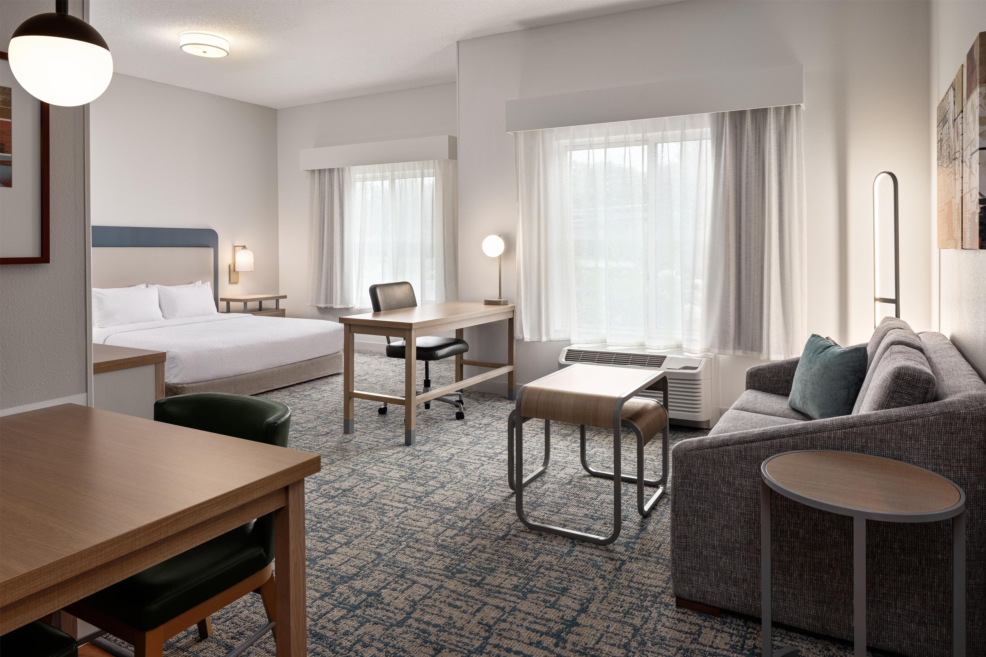 A hotel room with a bed, desk, chair, sofa, and a small table.