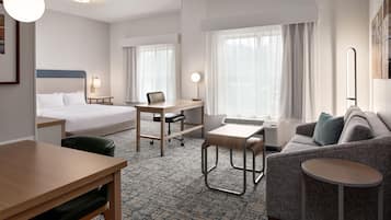 A hotel room with a bed, desk, chair, sofa, and a small table.