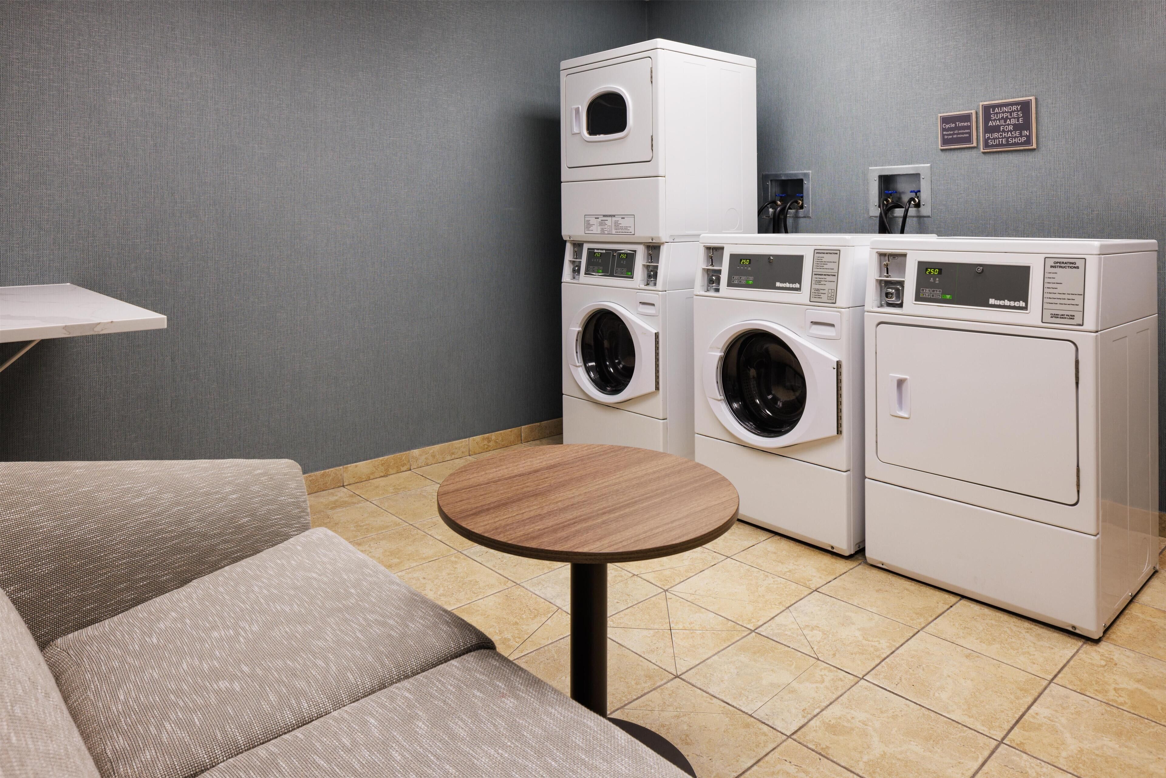 A laundry room with stacked washing machines, a small table, and a sofa.