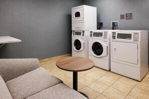 A laundry room with stacked washing machines, a small table, and a sofa. - Homewood Suites by Hilton Minneapolis/St. Paul-New Brighton (New Brighton)