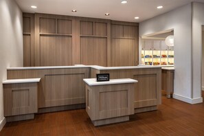 Zona de recepción de hotel con diseño de paneles de madera, un letrero que dice 'Hilton HONORS' y una vista de un minibar bien surtido.
