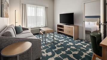 Une chambre d’hôtel avec un canapé, une petite table, un téléviseur, un lit et une moquette à motifs.