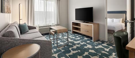 A hotel room with a sofa, a small table, a TV, a bed, and a patterned carpet.