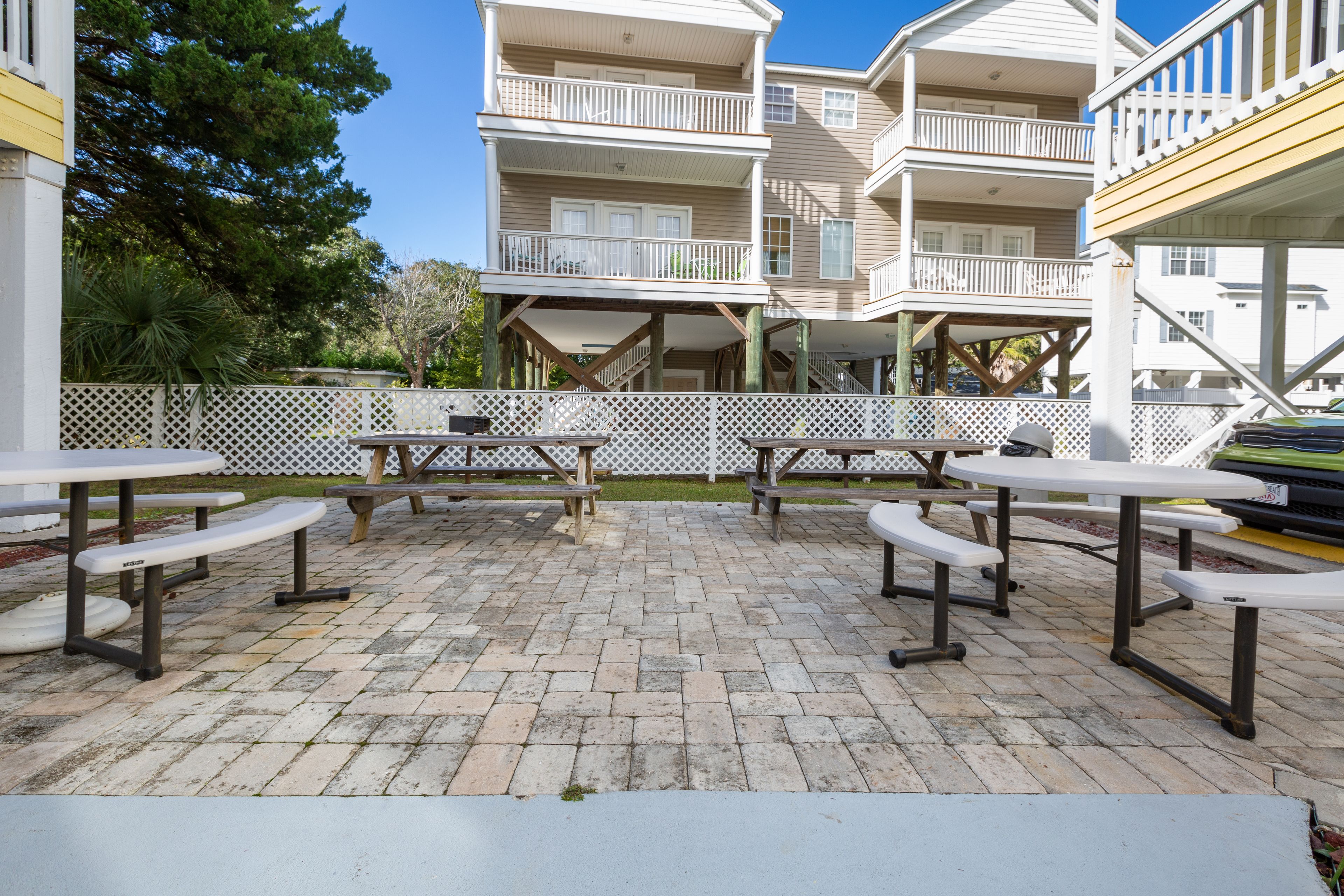 A patio area with picnic tables and a white fence.