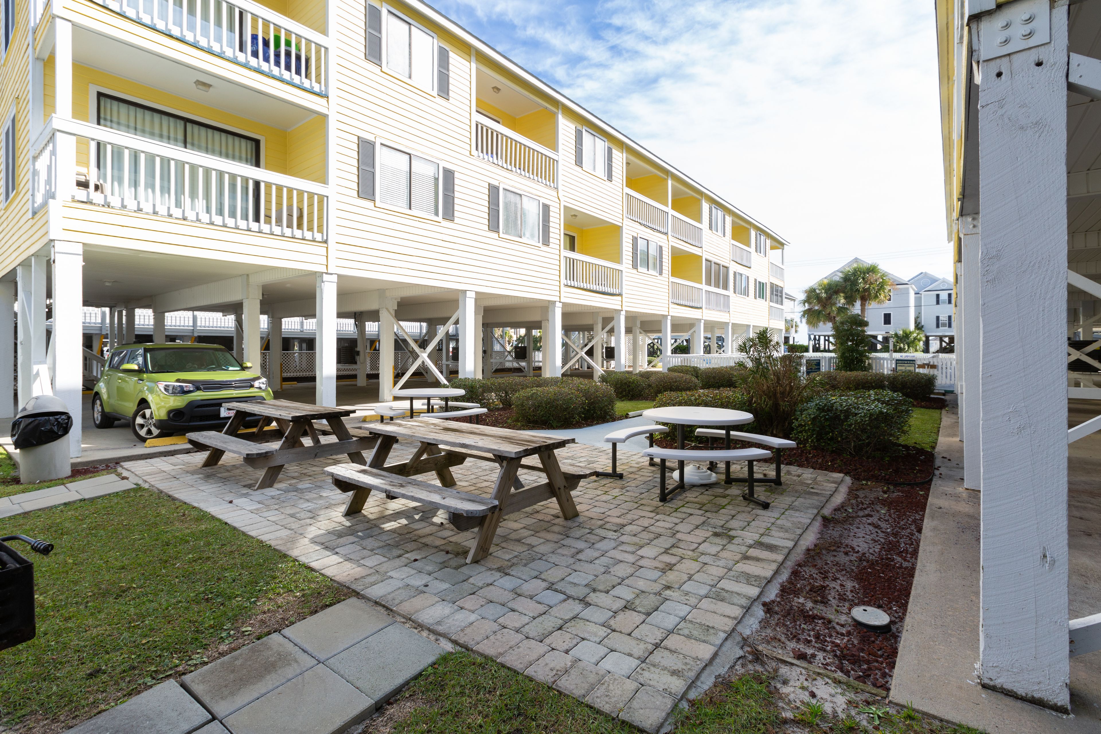 A multi-story hotel with outdoor picnic tables and a car parked in front.