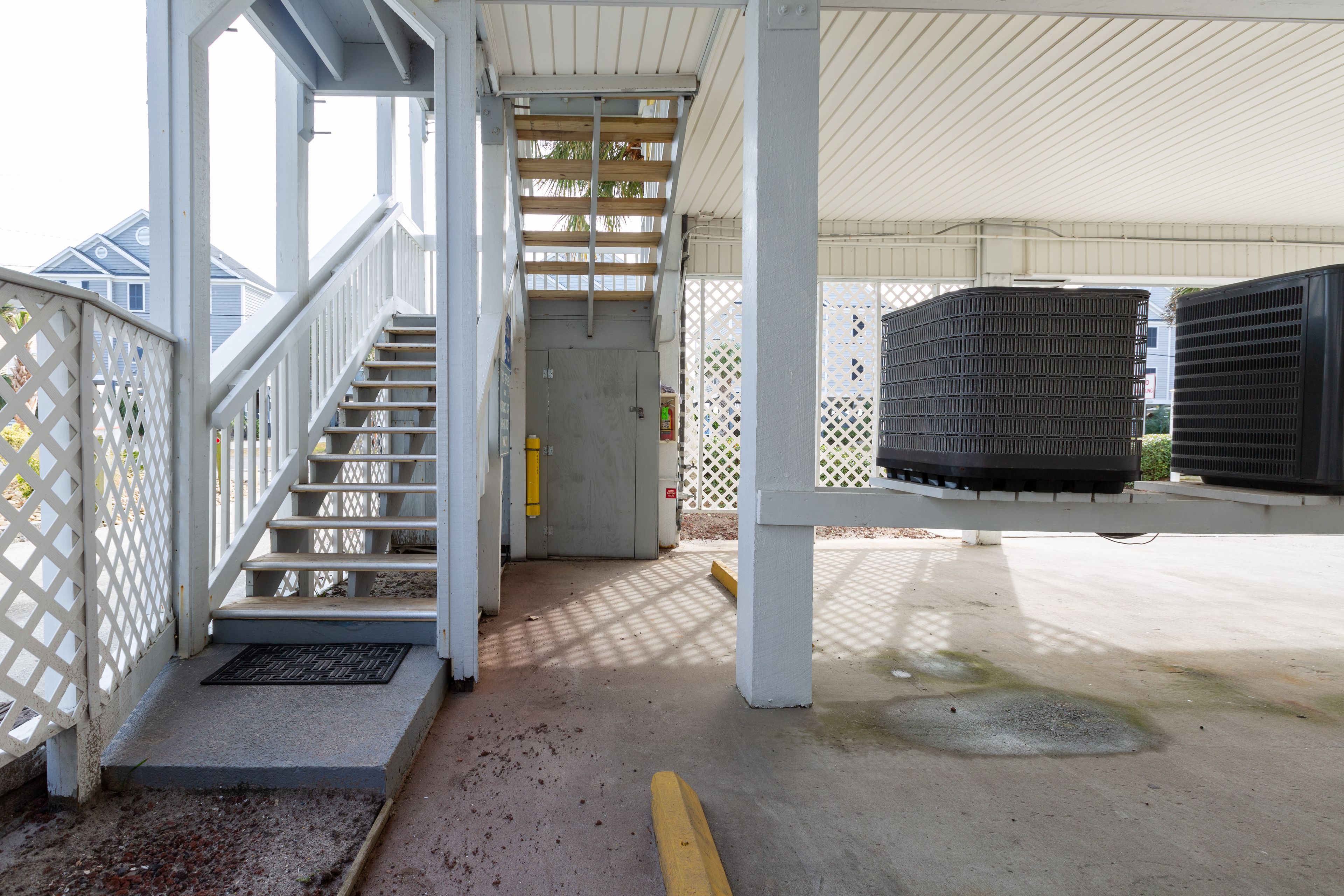 A covered outdoor area with a staircase leading to a door, concrete flooring, and a metal fence.