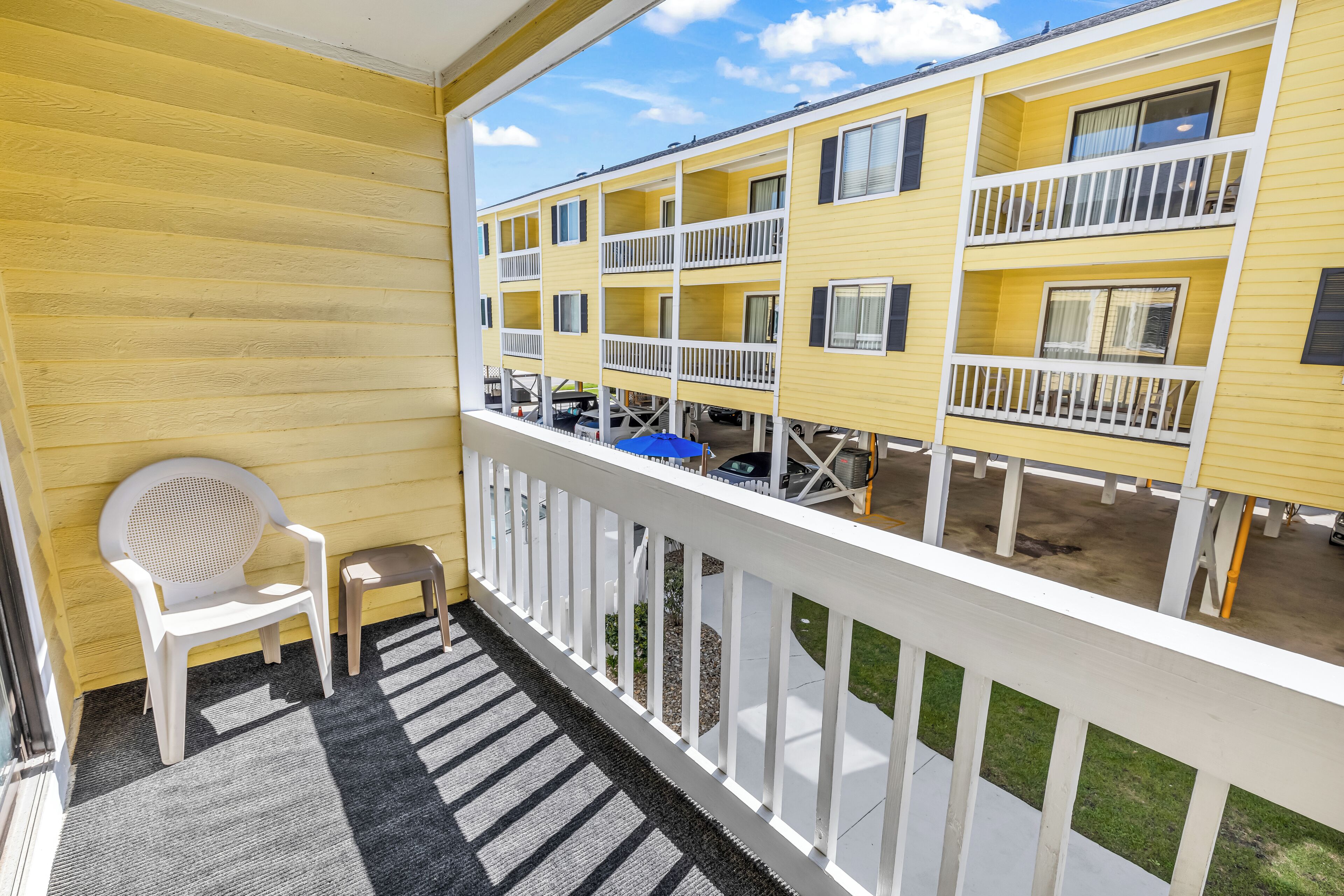 A balcony with a white chair and a small table, overlooking a yellow building with multiple balconies.
