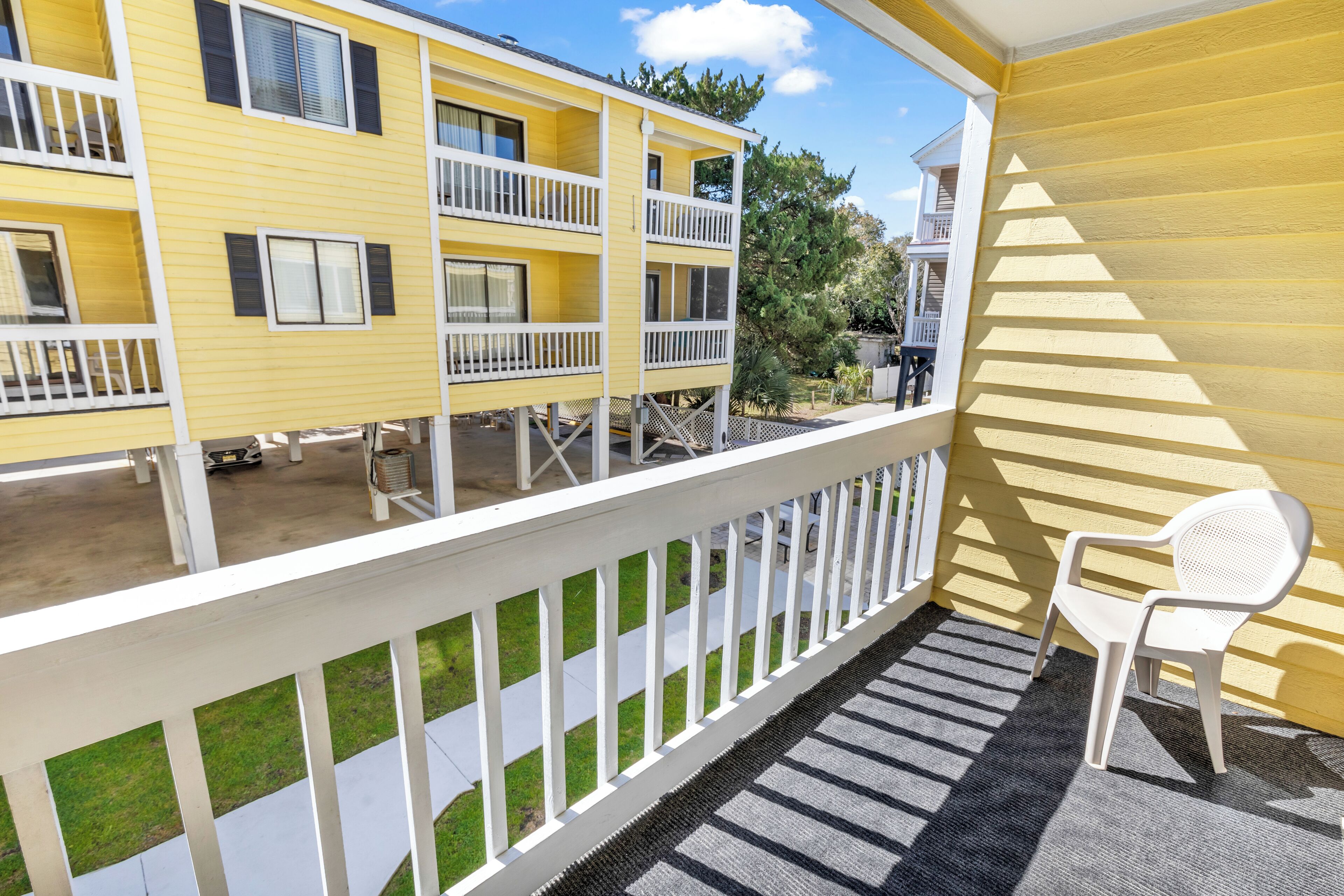 A yellow building with white railings and a white chair on a balcony.