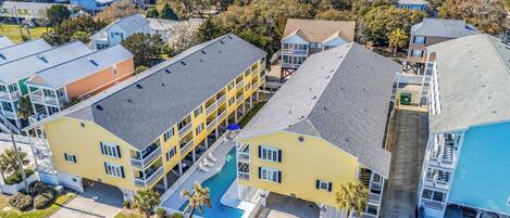 A multi-story hotel with balconies, a swimming pool, and a parking area.