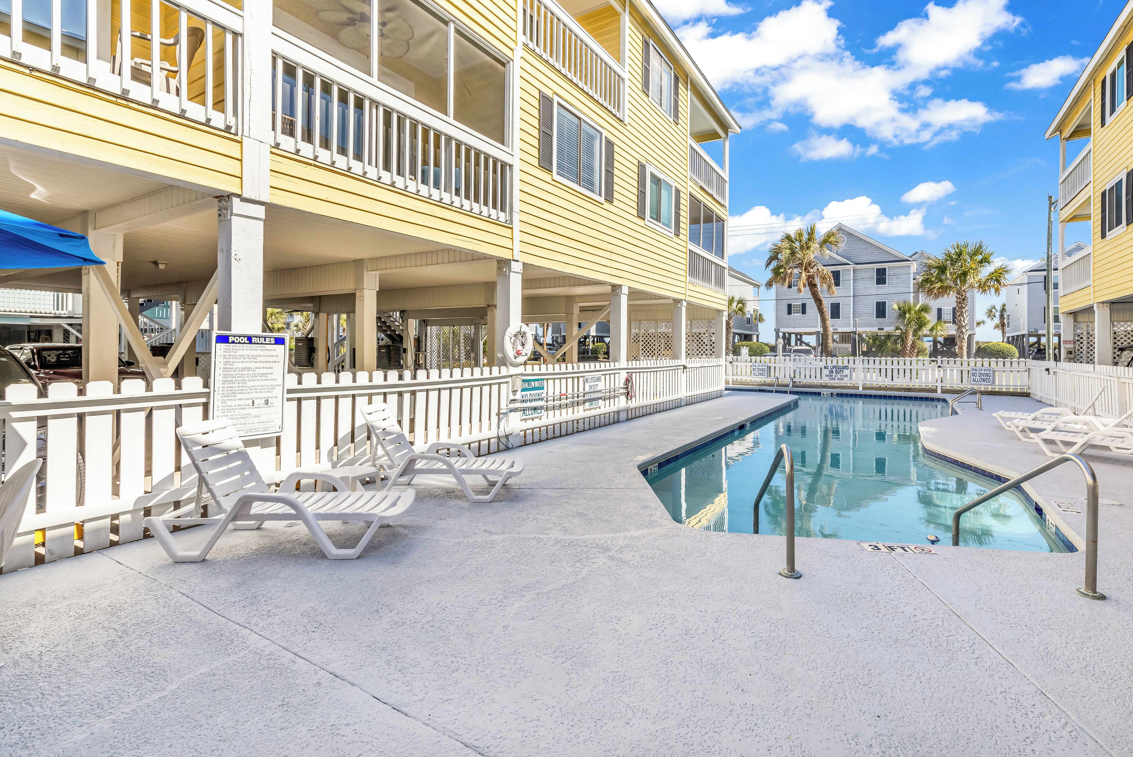 A pool area with lounge chairs and a sign indicating pool rules.