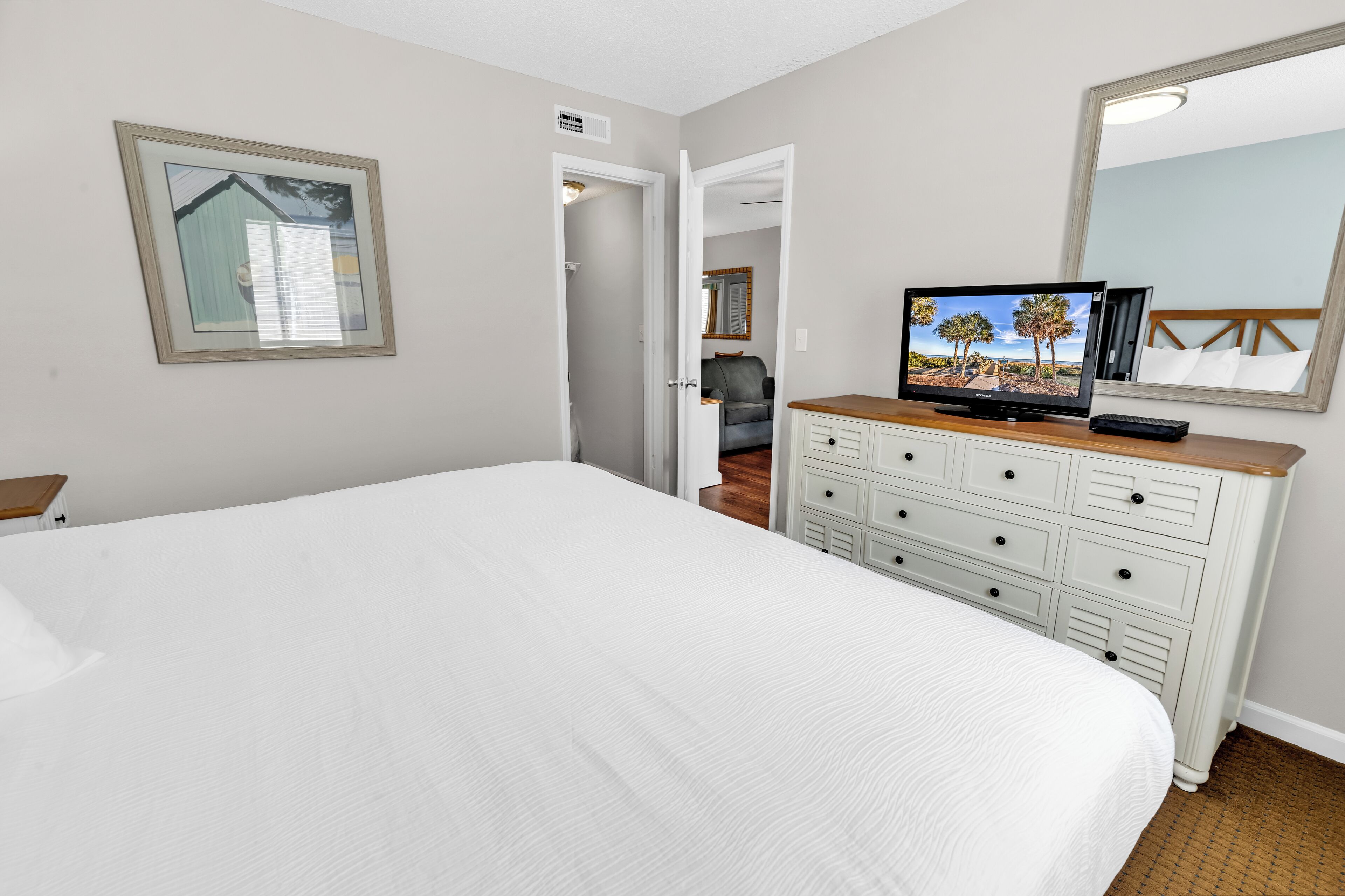 A bedroom with a large bed, a dresser, a television, and a mirror.