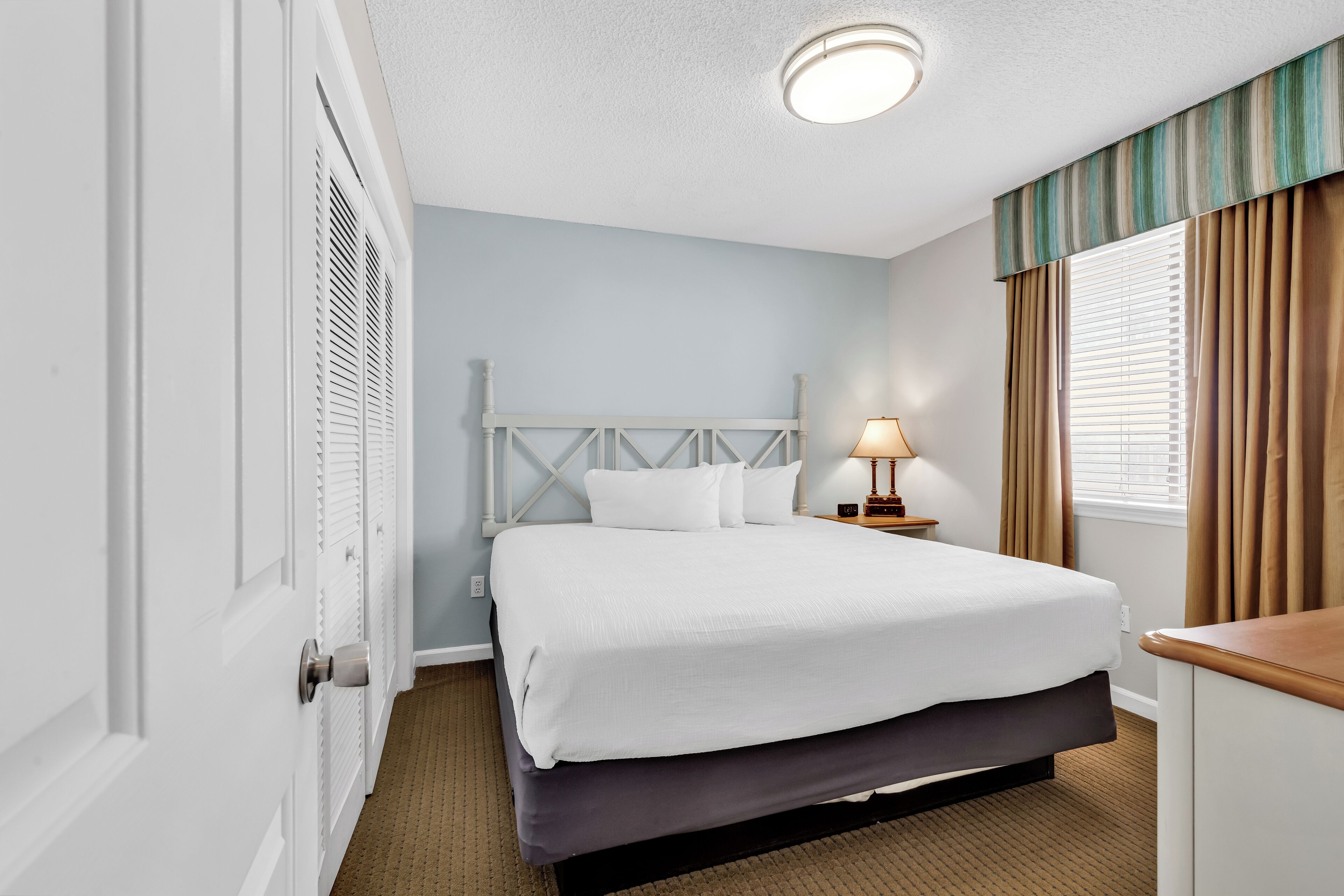 Une chambre d’hôtel avec un lit, une table de chevet, une lampe et une fenêtre avec des rideaux.