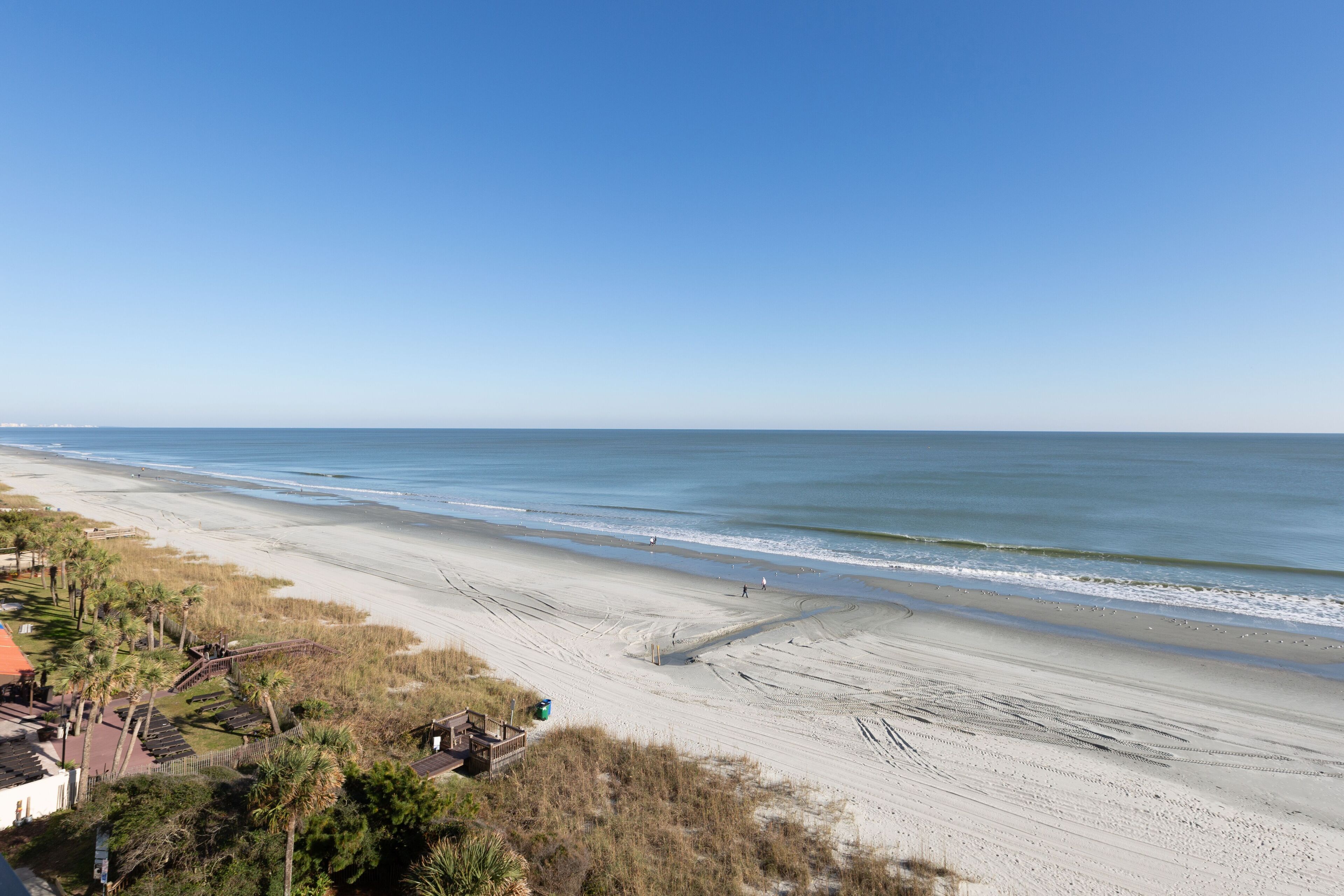 Een strand met een heldere lucht, zandstrand en enkele gebouwen op de achtergrond.