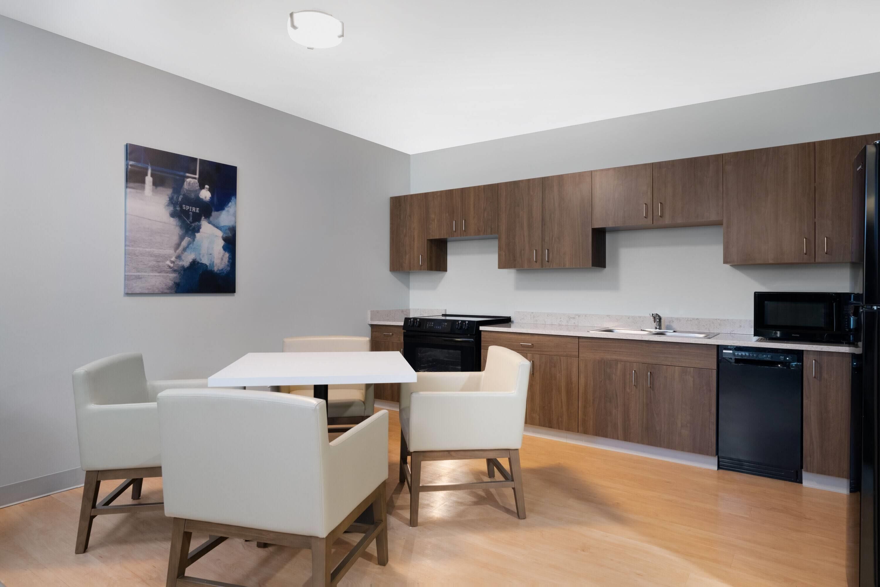 Una cocina moderna con armarios de madera, un refrigerador negro, lavavajillas y una mesa de comedor blanca con sillas.