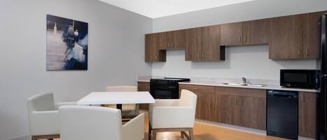Una cocina moderna con armarios de madera, un refrigerador negro, lavavajillas y una mesa de comedor blanca con sillas.