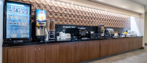 A modern self-service beverage station with a refrigerated display, a juice dispenser, and a coffee machine.