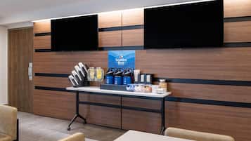 Un área de recepción de hotel moderna con un panel de pared de madera, dos televisores montados, un mostrador de recepción con servicios y una zona de estar.