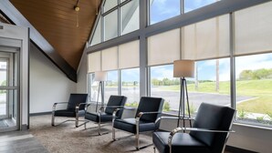Une salle d’attente avec quatre chaises noires, un lampadaire et de grandes fenêtres donnant sur un paysage verdoyant.