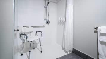 Un baño con ducha, baranda, una silla blanca y un perchero para toallas.