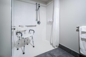 Un baño con ducha, baranda, una silla blanca y un perchero para toallas.
