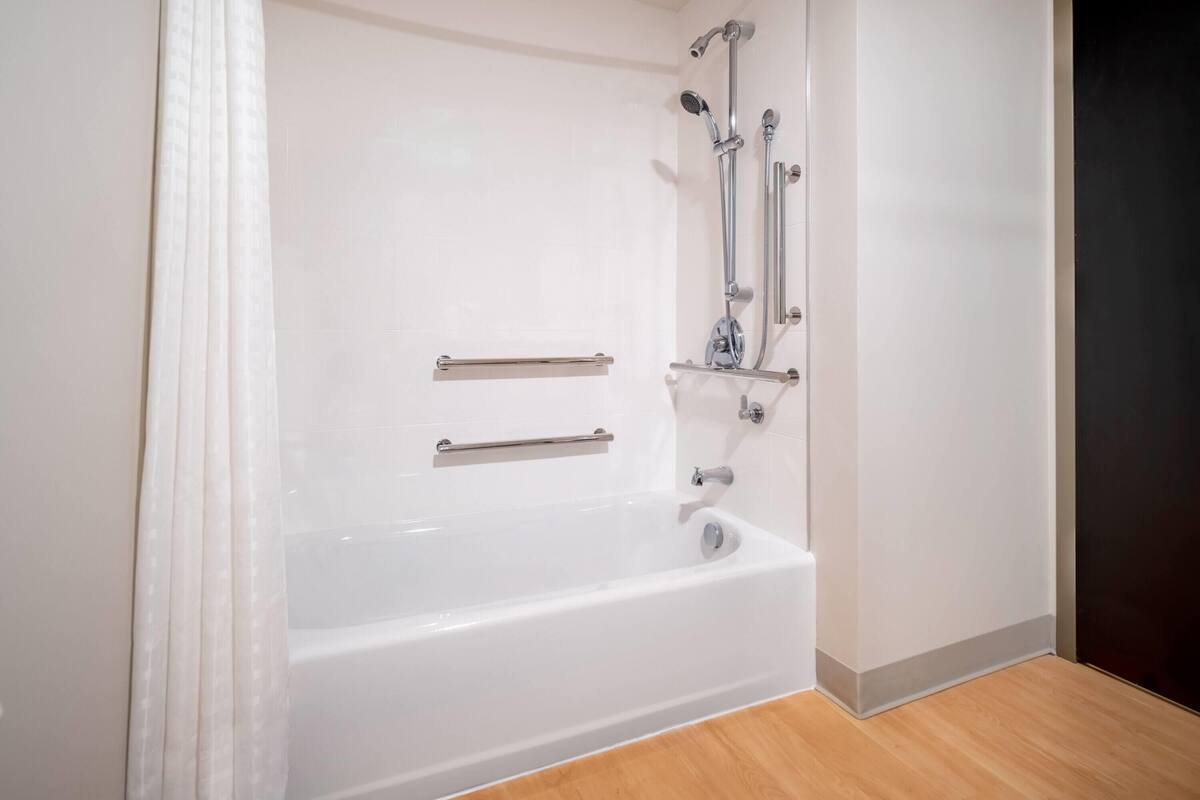 A white bathtub with grab bars, a showerhead, and a faucet.