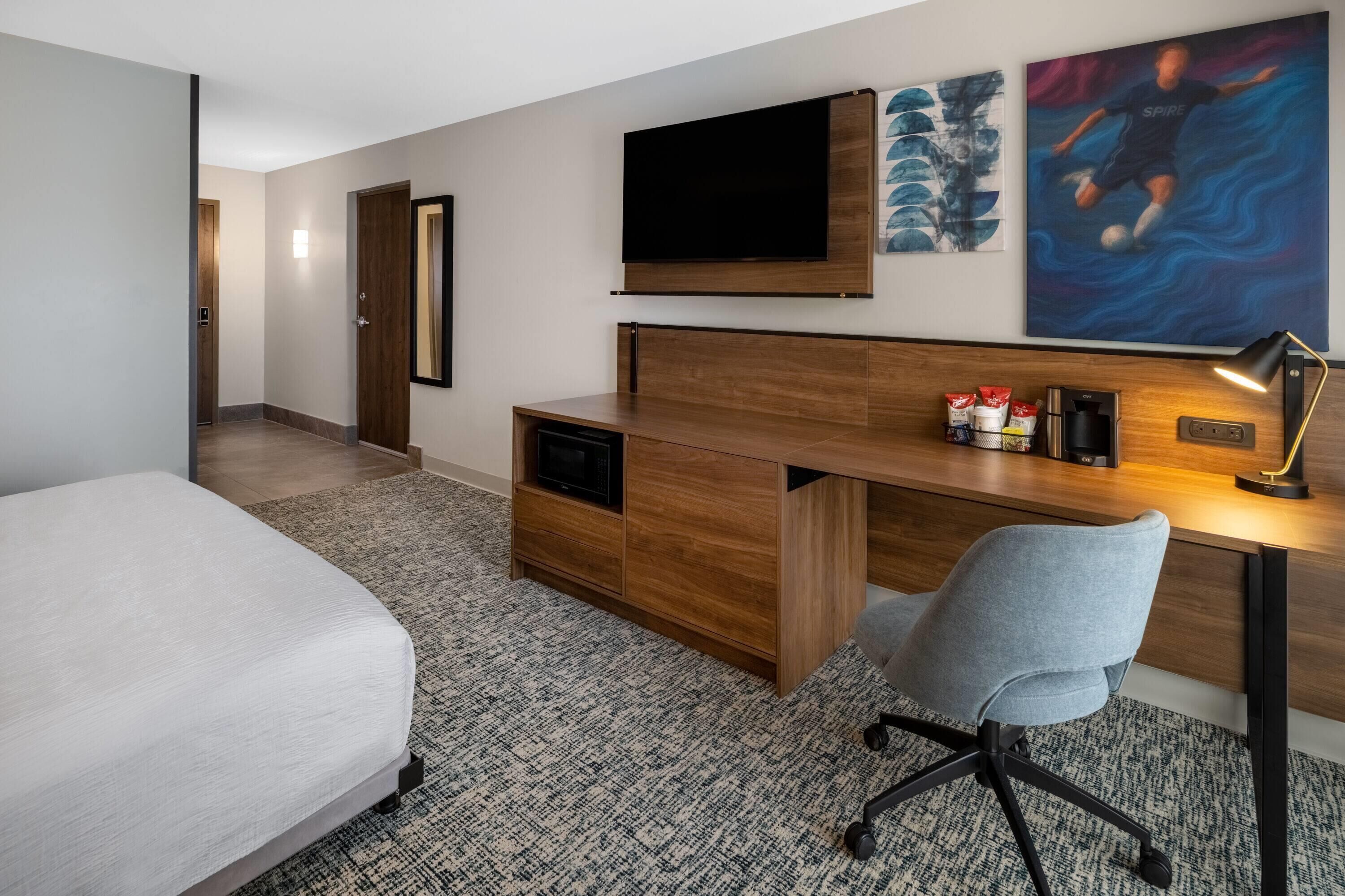Een hotelkamer met een bed, een bureau met een stoel, een televisie en kunst aan de muur.