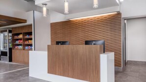 Un comptoir d’accueil avec un panneau décoratif en bois, un plan de travail blanc et deux écrans noirs.