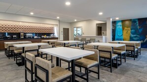 Un espace repas moderne avec plusieurs tables et chaises, une cuisine en arrière-plan et une fresque murale.
