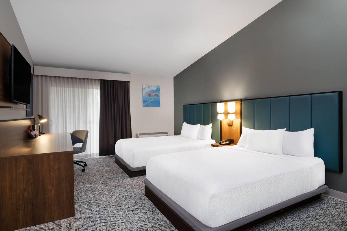 A hotel room with two beds, a desk, a television, and a painting on the wall.