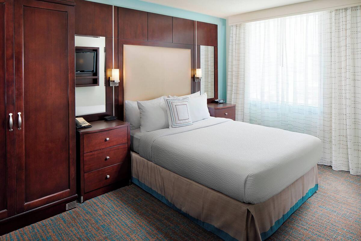 A hotel room with a large bed, wooden wardrobe, bedside table, lamp, and a television.